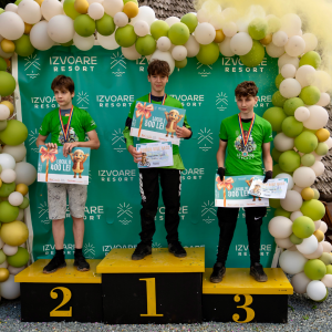 Three young male athletes stand on a yellow podium with 1st, 2nd, and 3rd places, holding prize certificates (500, 400, and 300 lei) under a balloon arch at Izvoare Resort.