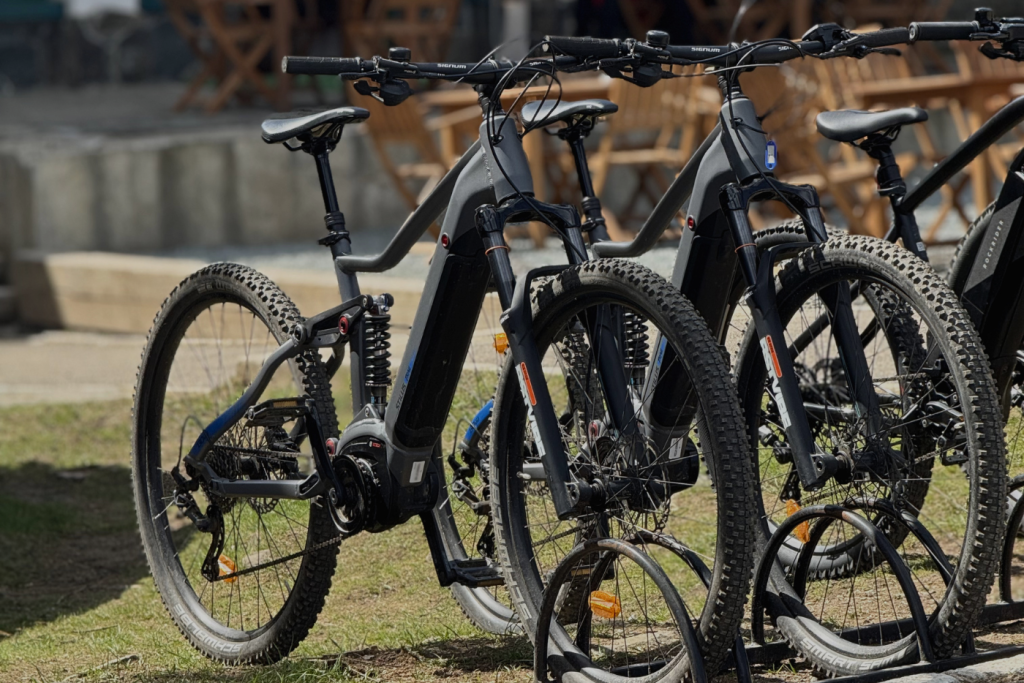 Row of black electric mountain bikes parked together with thick tread tires and front suspension forks, outdoors.