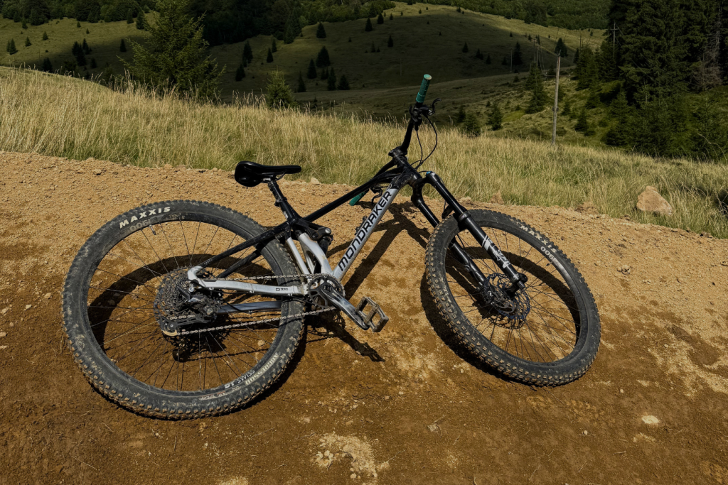 Black full-suspension mountain bike resting on a dirt trail with grassy hillside and trees in the background.